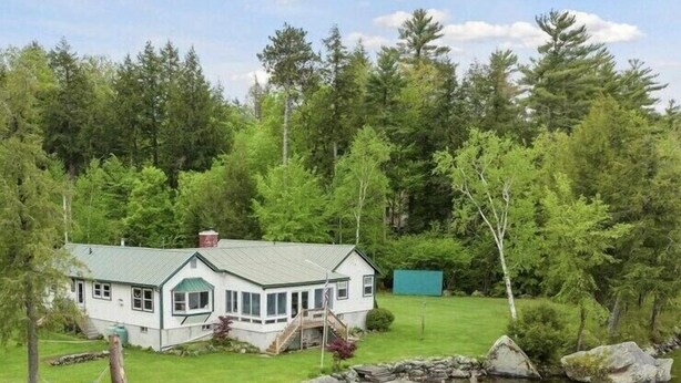Une maison avec un toit végétalisé, une véranda et une jetée qui s’avance sur un étang.
