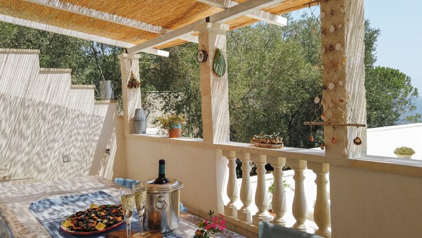 A covered outdoor dining area with a table set for two, a metal pot, and a potted plant. - Blue House (Castro)