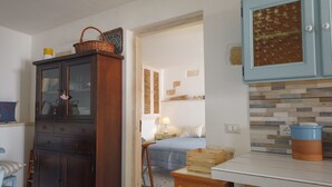 A room with a wooden cabinet, a bed with a blue bedspread, a nightstand with a lamp, and a wall with a textured backsplash. - Blue House (Castro)