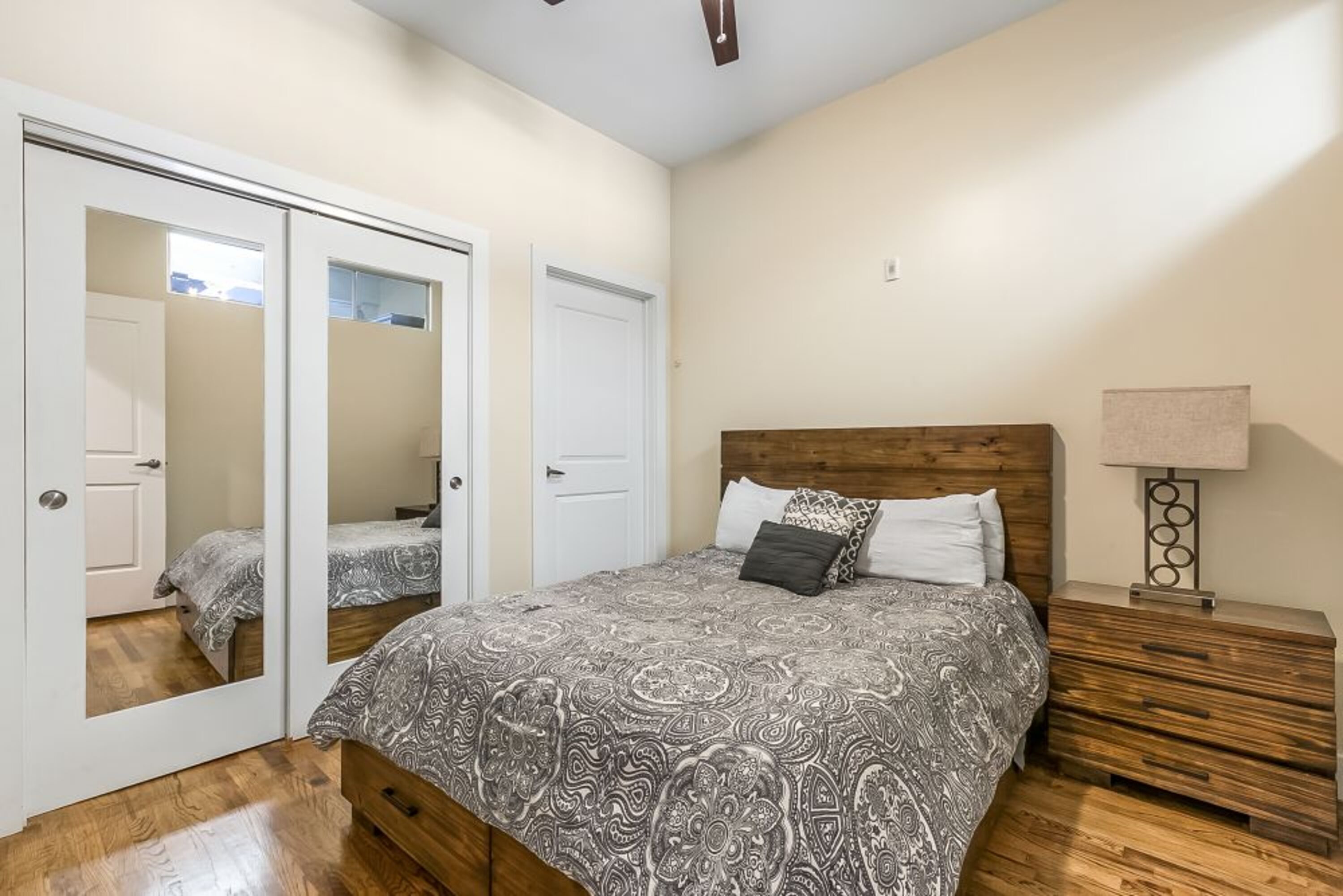 A bedroom with a bed, a nightstand, a mirror, and a door.
