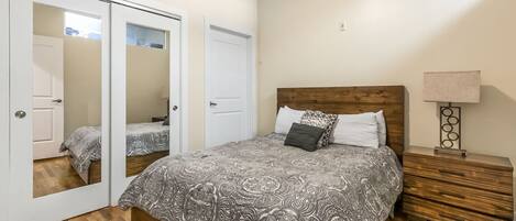 A bedroom with a bed, a nightstand, a mirror, and a door.