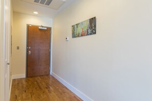 A hallway with a wooden floor, a closed door, and a wall-mounted painting. - Merchant Lofts Comfy Condos – Walk Everywhere (New Orleans)