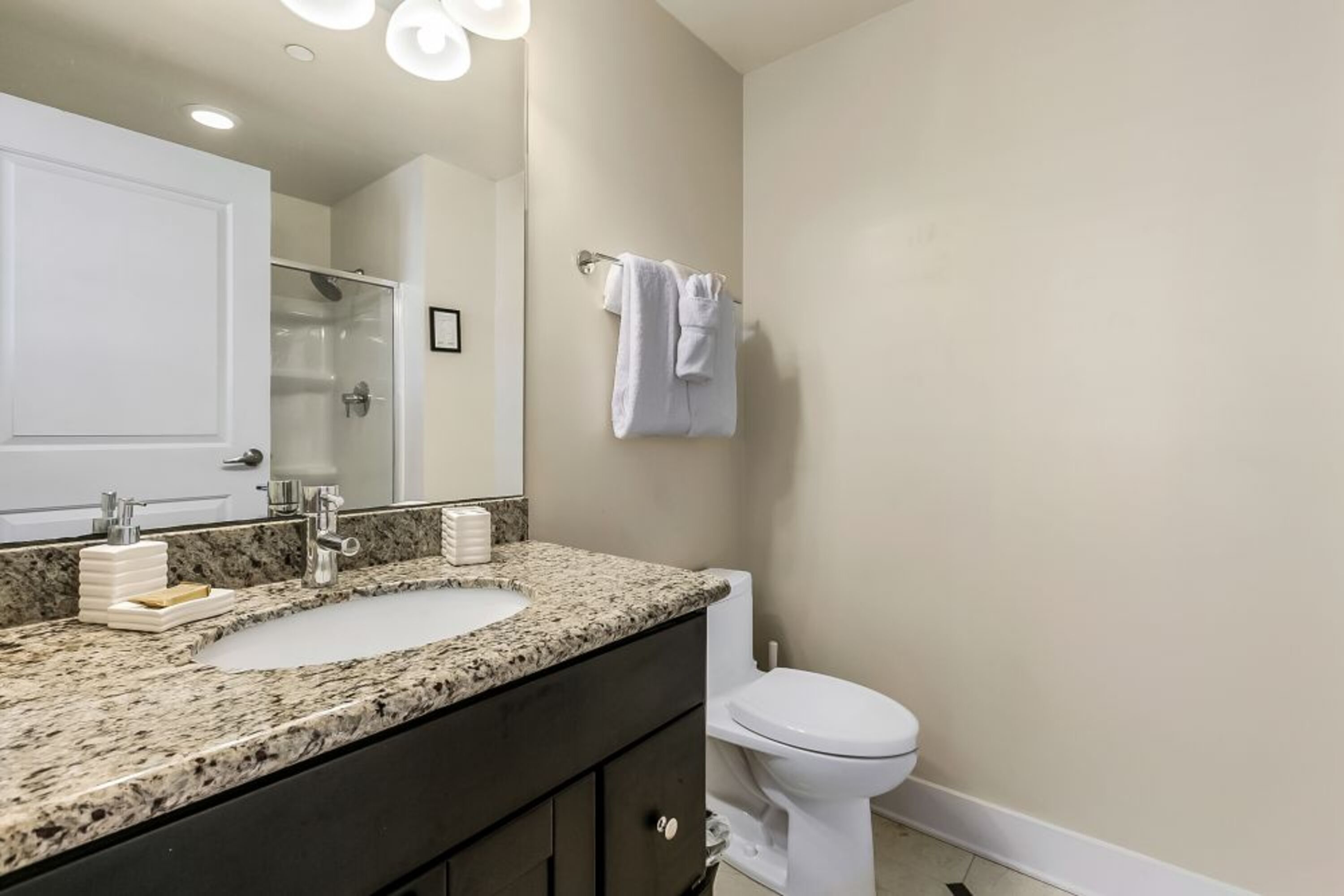A bathroom with a granite countertop sink, a white toilet, and a towel rack.