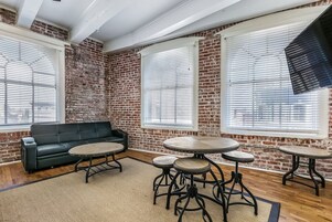 Una habitación con paredes de ladrillo visto, un sofá de cuero negro y tres mesas redondas con patas de metal.