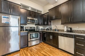 A modern kitchen with dark cabinets, stainless steel appliances, and a granite countertop. - Merchant Lofts Comfy Condos – Walk Everywhere (New Orleans)