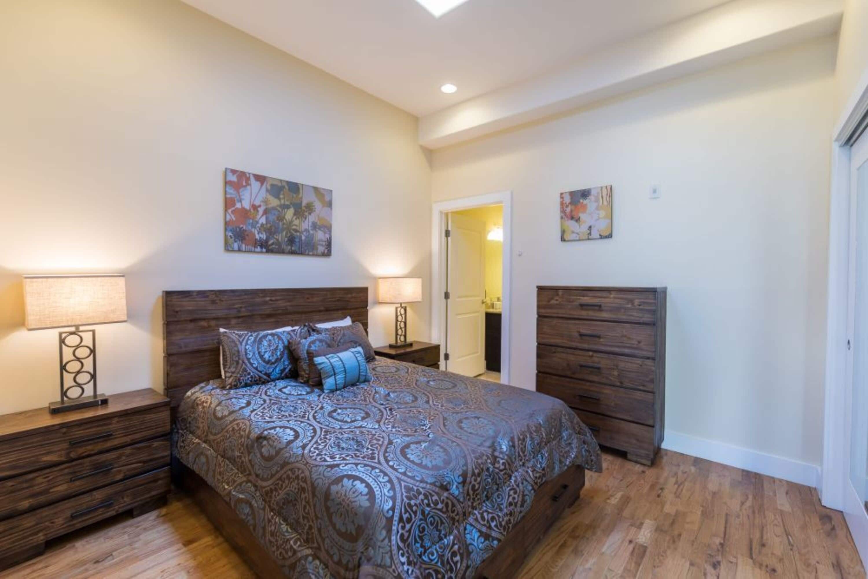 A bedroom with a large bed, wooden headboard, two nightstands with lamps, and a door leading to another room.