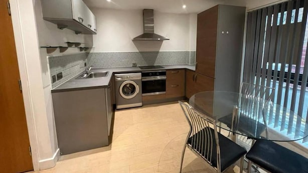 A compact kitchen with a washing machine, oven, and a glass dining table with chairs. - 1 Bedroom Flat - Lace Market Nottingham (Nottingham)