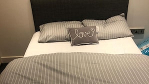 A neatly made bed with striped bedding and a pillow with 'love' written on it. - 1 Bedroom Flat - Lace Market Nottingham (Nottingham)
