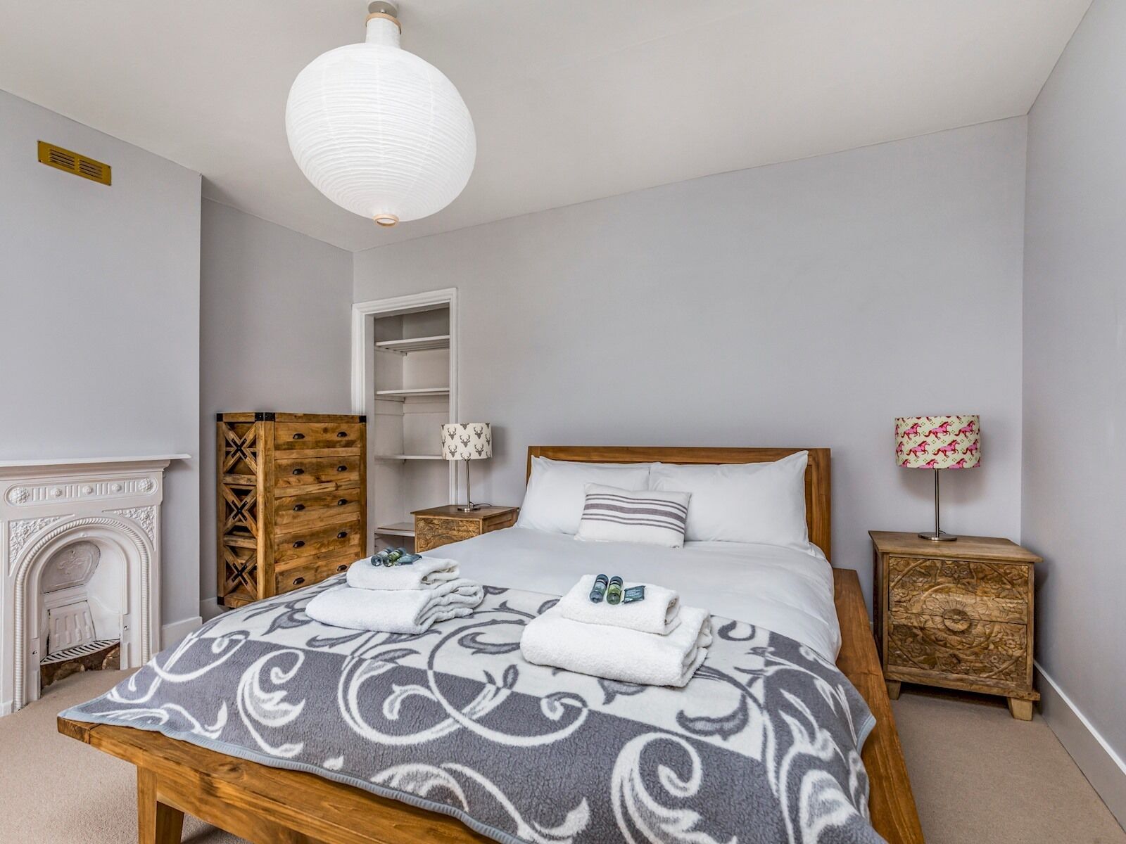 A neatly arranged bedroom with a bed, a wooden dresser, a nightstand, a lamp, and a fireplace.