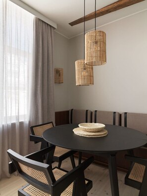 Een eetgedeelte met een ronde tafel, zwarte stoelen met gevlochten zittingen en een hanglamp met gevlochten details.