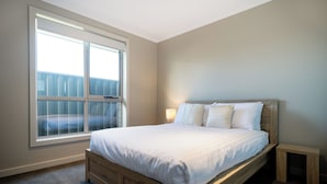 A bedroom with a large window, a wooden bed, a bedside table, and a nightstand. - Cute & Cosy 2 Bedroom Unit with Parking & WiFi (Prospect)