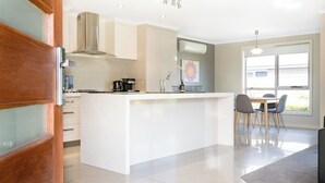 A modern kitchen with a central island, a dining area with chairs, and a large window providing natural light. - Cute & Cosy 2 Bedroom Unit with Parking & WiFi (Prospect)