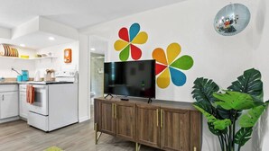 A modern kitchen with white cabinetry, a built-in oven, and a wooden cabinet with a flat-screen TV. - That 70s Themed Apt Close to Coffee, Food and Shops (Tampa)