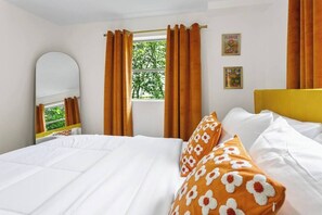 A bedroom with a bed, a window with curtains, a mirror, and a wall with two framed pictures. - That 70s Themed Apt Close to Coffee, Food and Shops (Tampa)