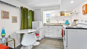A compact kitchen with white cabinets, a dining table with two chairs, a small refrigerator, and a stove. - That 70s Themed Apt Close to Coffee, Food and Shops (Tampa)
