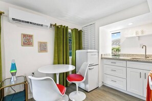 A compact kitchen with a white refrigerator, a small dining table with two chairs, and a window with green curtains. - That 70s Themed Apt Close to Coffee, Food and Shops (Tampa)