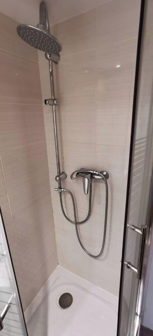 Un box de ducha con paredes de vidrio, equipado con un cabezal de ducha manual y un accesorio de ducha manual.