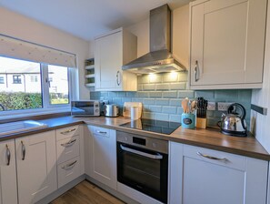 A modern kitchen with white cabinets, a stainless steel range hood, a toaster, and a kettle on the countertop. - Parkview Cottage - Beautiful terraced bungalow with cosy fireplace (Carnoustie)