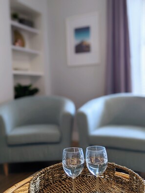 A room with two light blue armchairs, a wicker table with two clear glasses of water, and a framed picture on the wall. - Parkview Cottage - Beautiful terraced bungalow with cosy fireplace (Carnoustie)