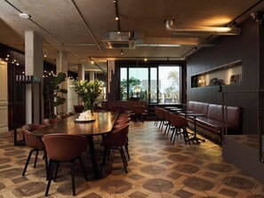 Un interior moderno con una amplia mesa de comedor, diversas opciones de asiento y vistas a través de grandes ventanales.
