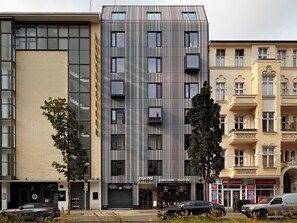 Een modern gebouw met een verticaal gestreept gevel, een koffiezaak op de begane grond, en aangrenzende oudere gebouwen.