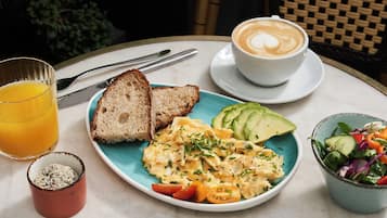 Un desayuno con tostadas, huevos revueltos, aguacate, una ensalada, una taza de café y un vaso de jugo de naranja.