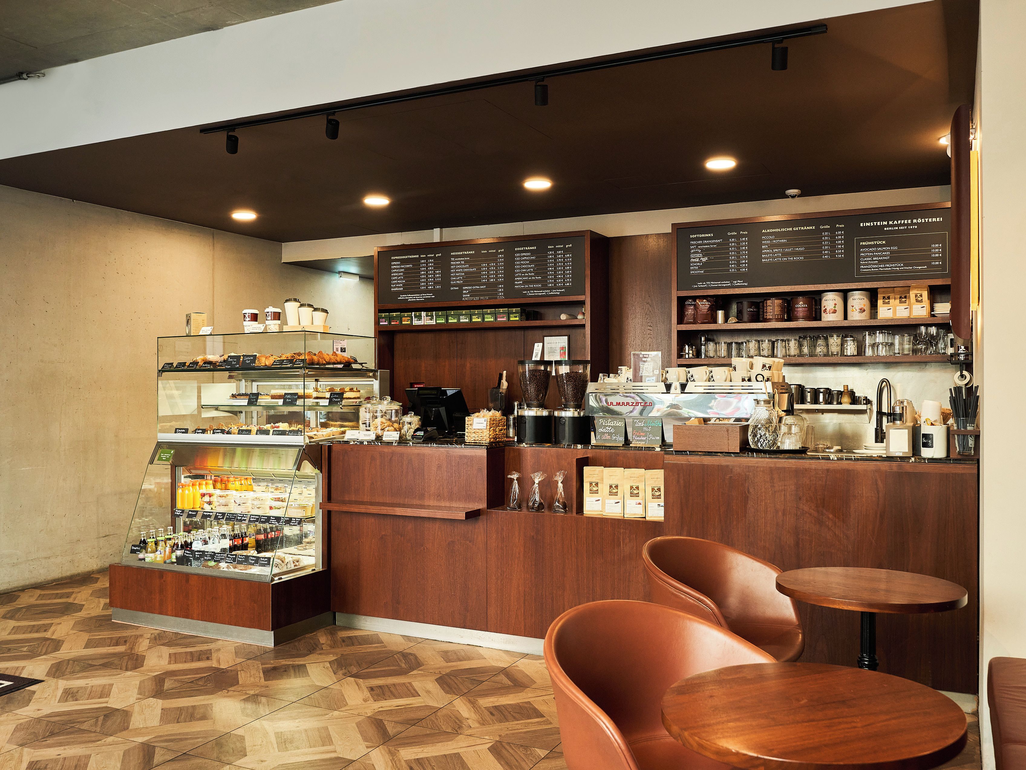 Interior de una cafetería con mostrador, zona de mesas y carteles de menú.