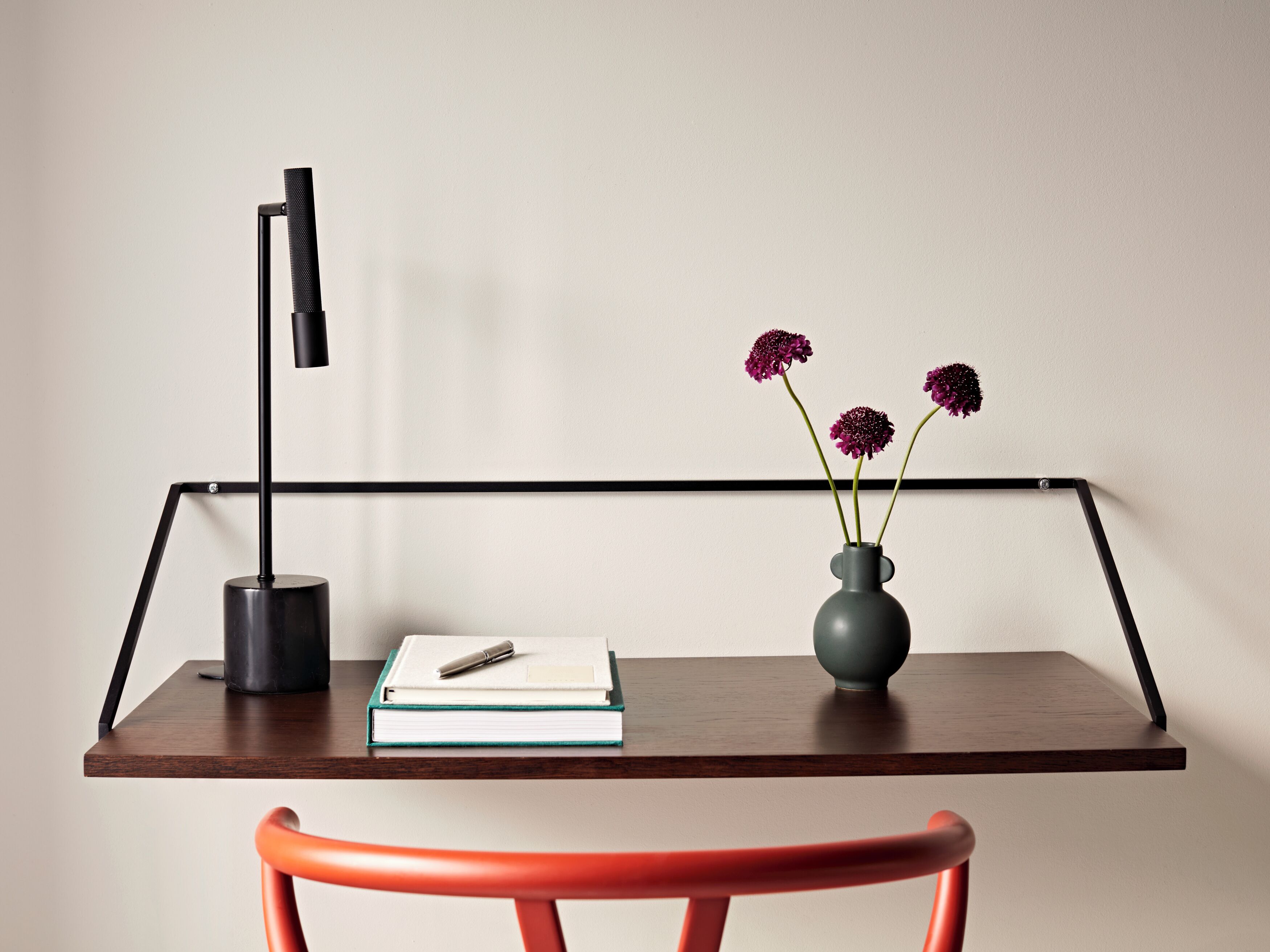 A desk with a lamp, a vase with flowers, a book, and a pen.