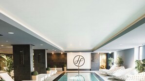 Een moderne binnenzwembadruimte met loungebedden, een centraal logo en een stenen muur.