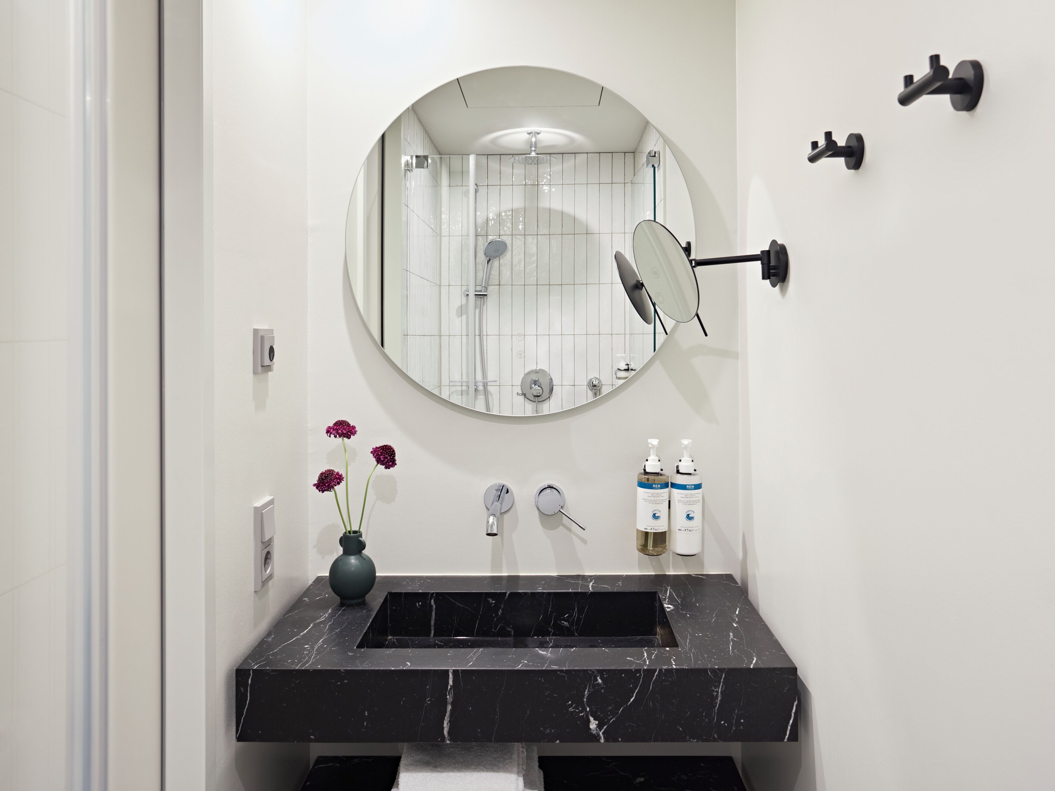 Un baño con lavamanos de mármol negro, un espejo redondo y una ducha.