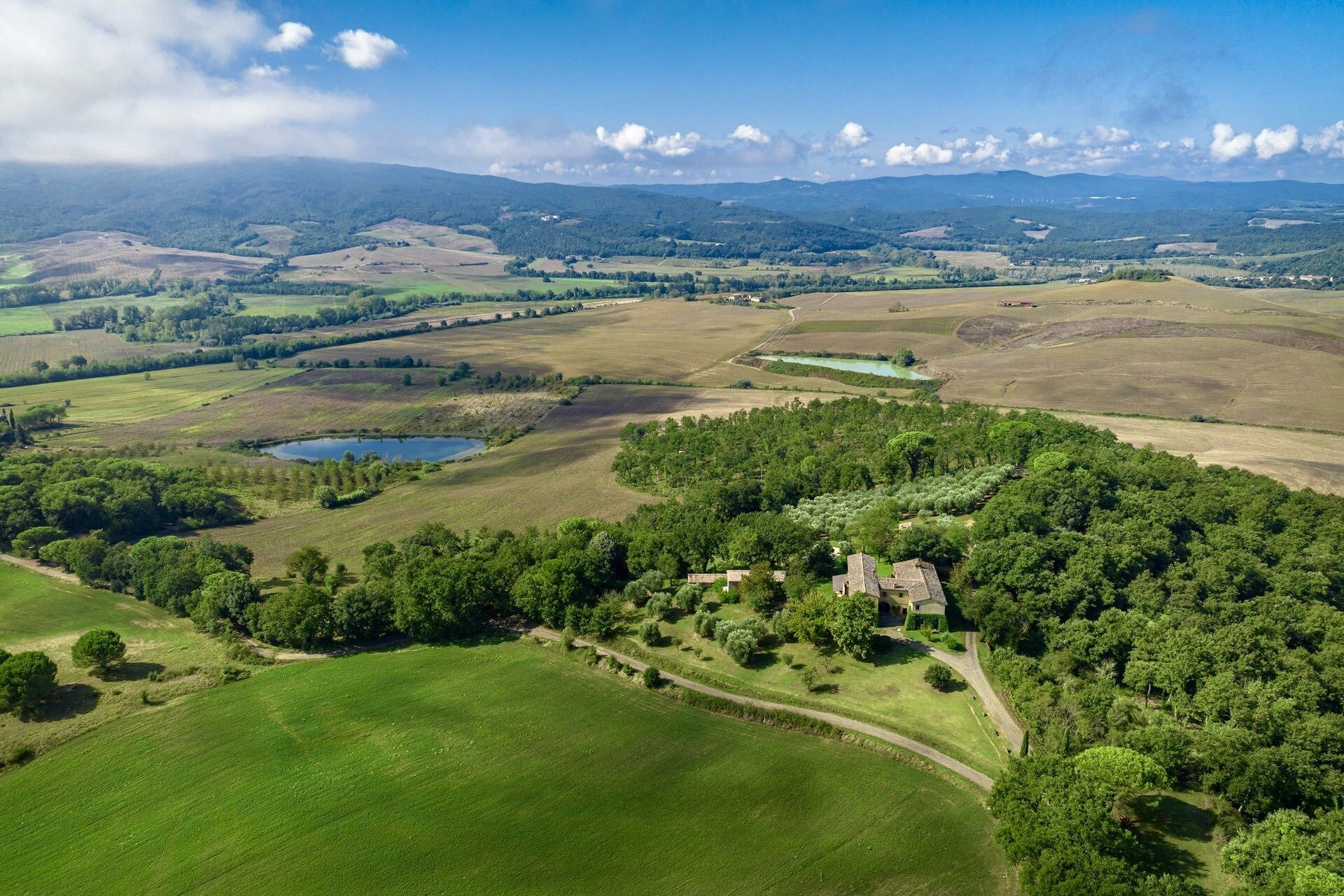 Vista aérea de un paisaje rural con colinas ondulantes, un lago pequeño y árboles dispersos.