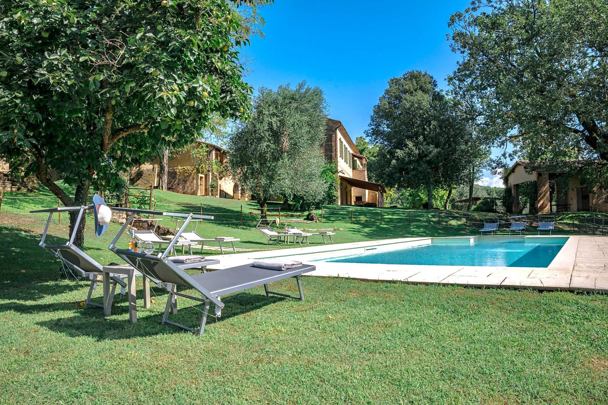 Une zone avec une piscine, des chaises longues, un ciel d’un bleu éclatant et un bâtiment en arrière-plan.