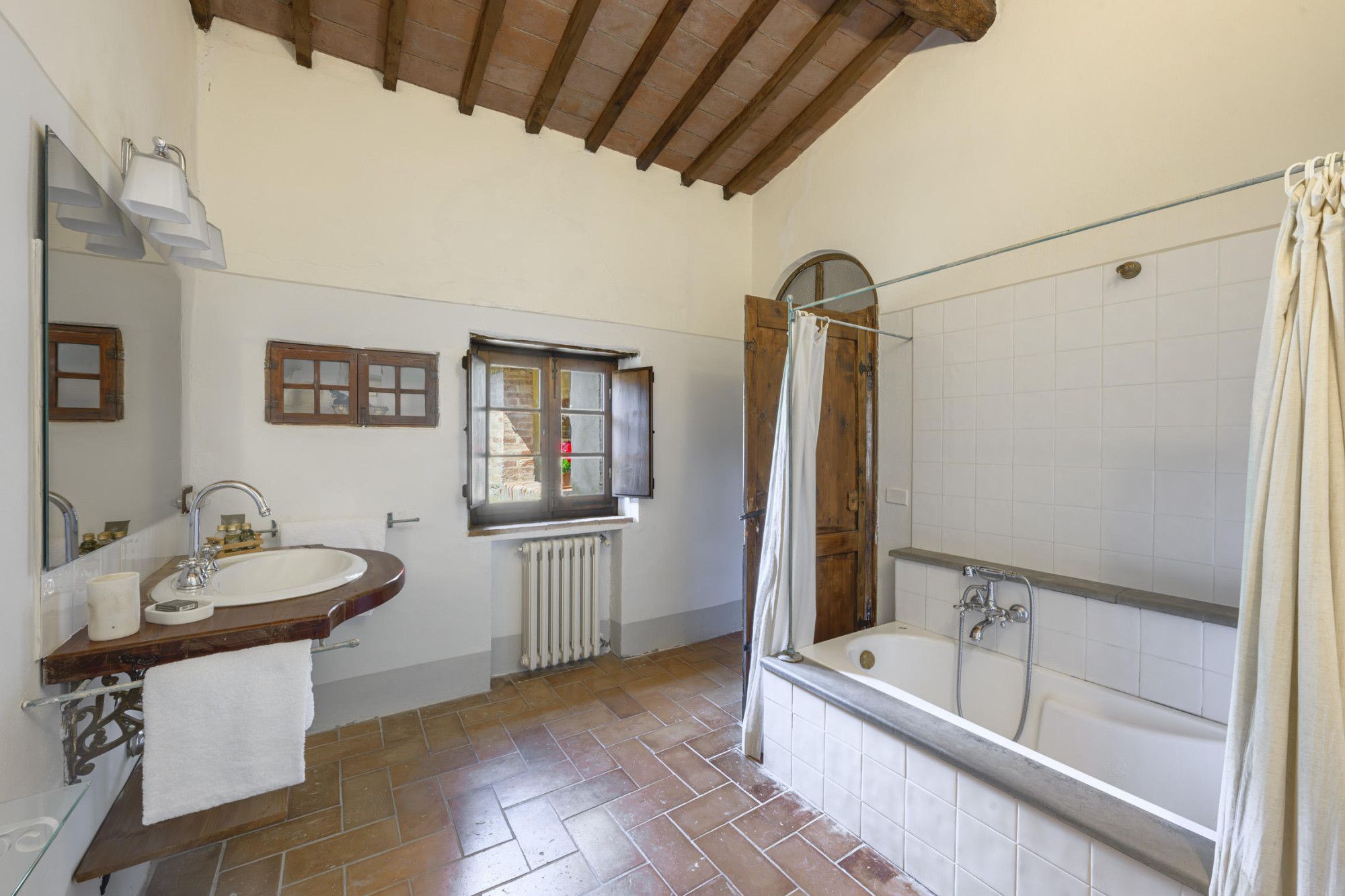 Un baño con techo de vigas de madera, una bañera, un lavamanos y un ventanal con vistas.