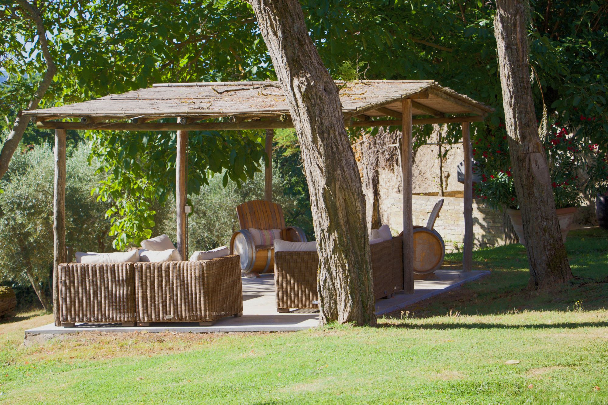 Une pergola en bois, agrémentée de meubles en osier et d’une barrique.