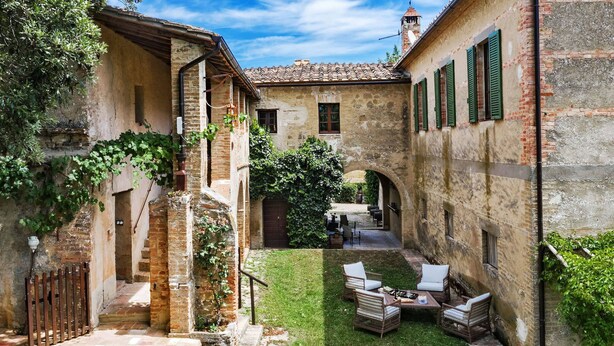 A courtyard with a grassy area, wicker furniture, and a brick building with green shutters. - BORGO ANTICO - Nine Bedroom Villa, Sleeps 20 (Montalcino)