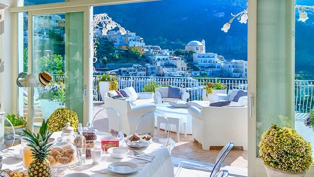 A dining area with a table set for breakfast, overlooking a coastal town with white buildings and blue sea. - VILLA BIANCA POSITANO (Positano)