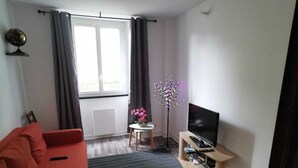 A modern living room with a red sofa, a TV on a wooden stand, a small table with a flower, and a globe on the wall.