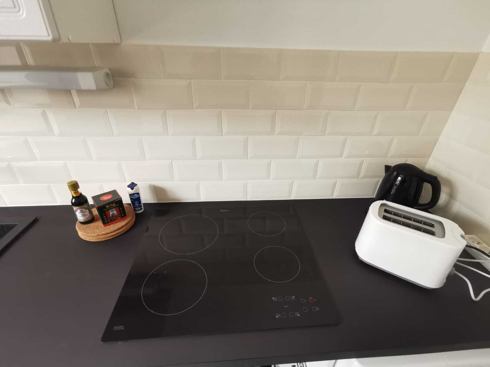 Eine Küche mit einer schwarzen Induktionskochplatte, einem weißen Toaster und einer Olivenölflasche auf einem Holzboden.