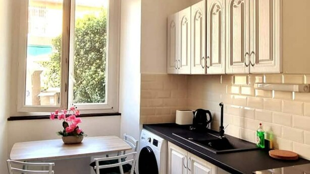 A kitchen with white cabinets, a black countertop, a window with a view of greenery, and a table with chairs.