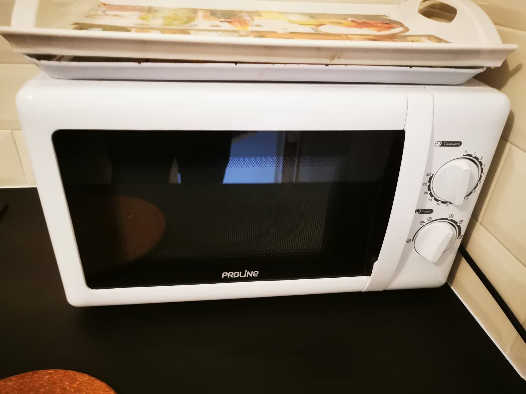 Eine weiße Mikrowelle mit digitaler Zeitanzeige und Power-Taste auf einer schwarzen Arbeitsfläche.