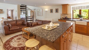 A spacious living area with a brown leather sofa, a kitchen with wooden cabinets, a granite countertop, and a dining area with a table and chairs. - Harthanger View Cottage, Luxborough (Wiveliscombe)
