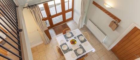 A dining area with a table set for six, a staircase, and a view of the outside.
