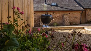 A wooden building with a brick wall, a chimney, and a barbecue grill in the foreground. - Harthanger View Cottage, Luxborough (Wiveliscombe)