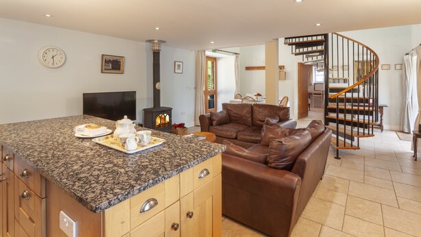 A kitchen with granite countertops, a built-in stove, and a dining area with a brown leather sofa. - Harthanger View Cottage, Luxborough (Wiveliscombe)