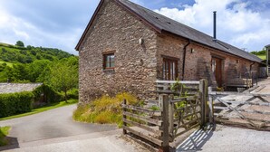 A stone building with a wooden door and window, surrounded by a stone wall and a wooden gate. - Harthanger View Cottage, Luxborough (Wiveliscombe)