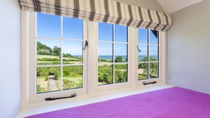 Una habitación con un ventanal grande, una colcha morada y vistas a un paisaje verde.