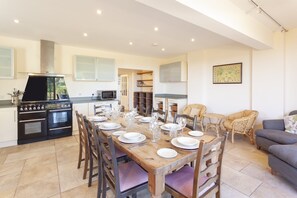 Un comedor con una mesa de madera dispuesta para seis personas, rodeada de sillas, y una cocina al fondo.
