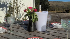 A wooden table with a white vase containing pink roses, a bottle of champagne, and several glassware items.