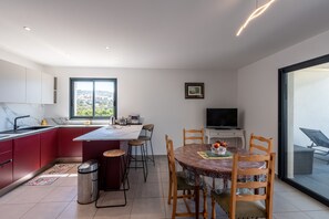 A modern kitchen with red cabinets, a dining area with a round table and chairs, a TV, and a large window offering a city view.