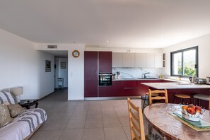 A modern kitchen with a central island, a dining area with a table and chairs, and a living area with a sofa and a lamp.